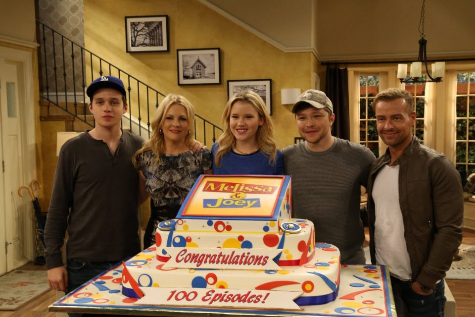 The cast of Melissa and Joey celebrates their 100th episode. Photo from Facebook. Photographs by Keith Dotson can be seen on the stairs.