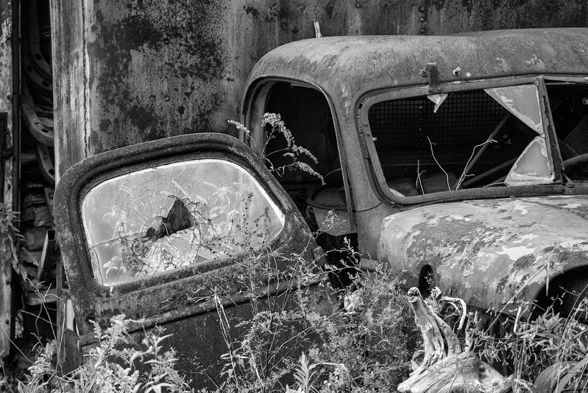 Broken windows on a rusty antique truck, abandoned in an overgrown meadow.
