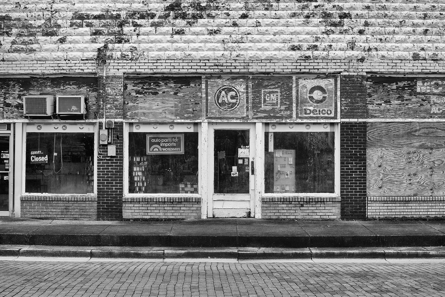 Black and white photograph of an old auto parts storefront Shadows