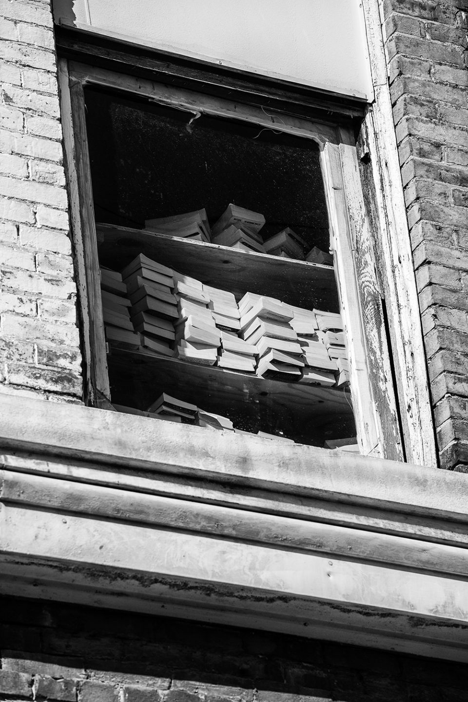 Stacks of books on a shelf on the second floor of an abandoned building. Black and white photograph by Keith Dotson.