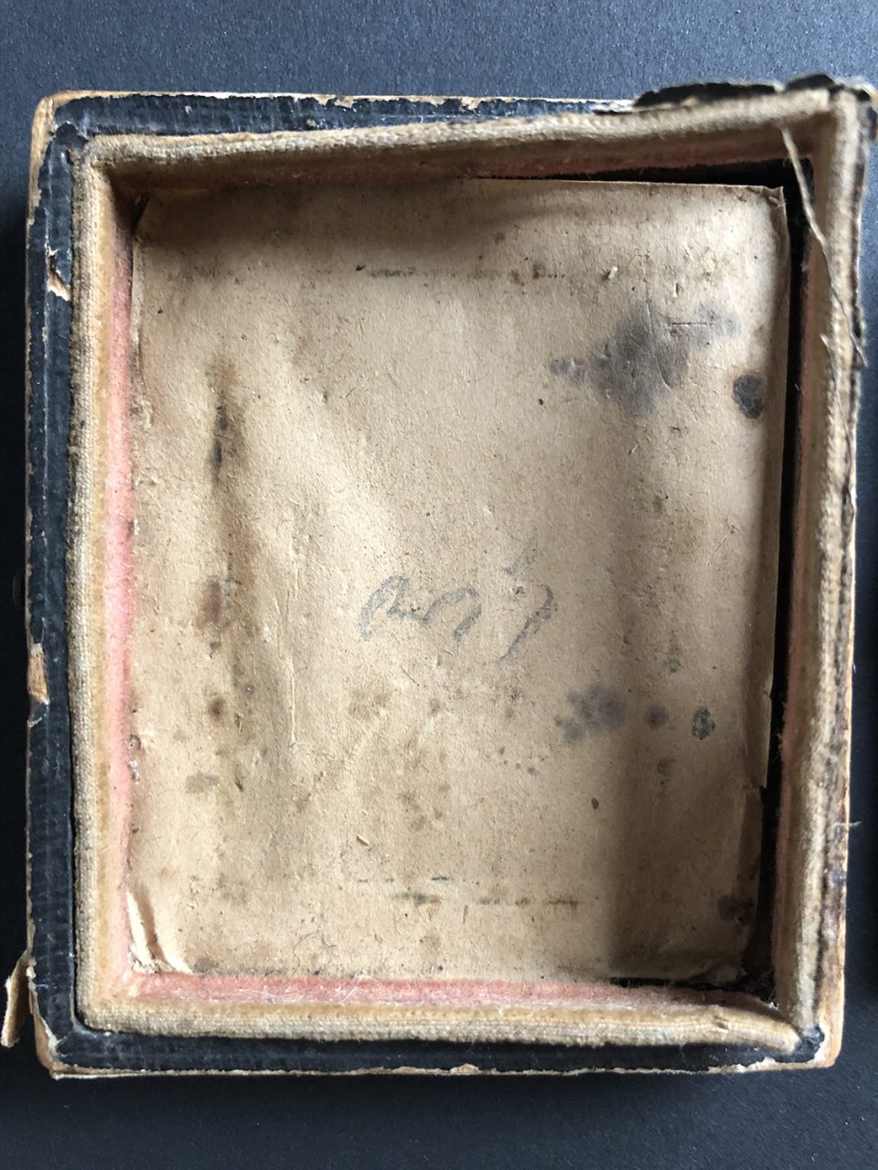 Close-up look at the interior of the tintype case. It's a wooden box with a paper liner and the thick paper (or possibly fabric) seal around the inner edges. Note the "1.00" handwritten in pencil on the paper . . . the hand of a stranger from 160 years ago, not seen by anyone since.