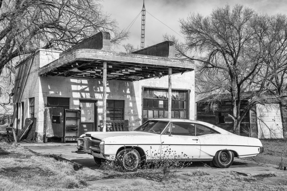 Black and white photograph of the vacant Brownlee Texaco Station, built in 1950, with a Pontiac Catalina parked in front. Accounts claim that in the heyday of Route 66, cars would wait in line for gasoline here. The station closed in the mod-70s after Interstate 40 opened, killing traffic on old Route 66 through town. Buy a print here.