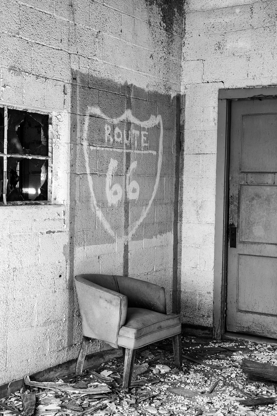 Black and white photograph of a chair beneath a hand-painted Route 66 sign, inside the abandoned Texas Longhorn Motel on Route 66 in Glenrio ghost town, Texas.
