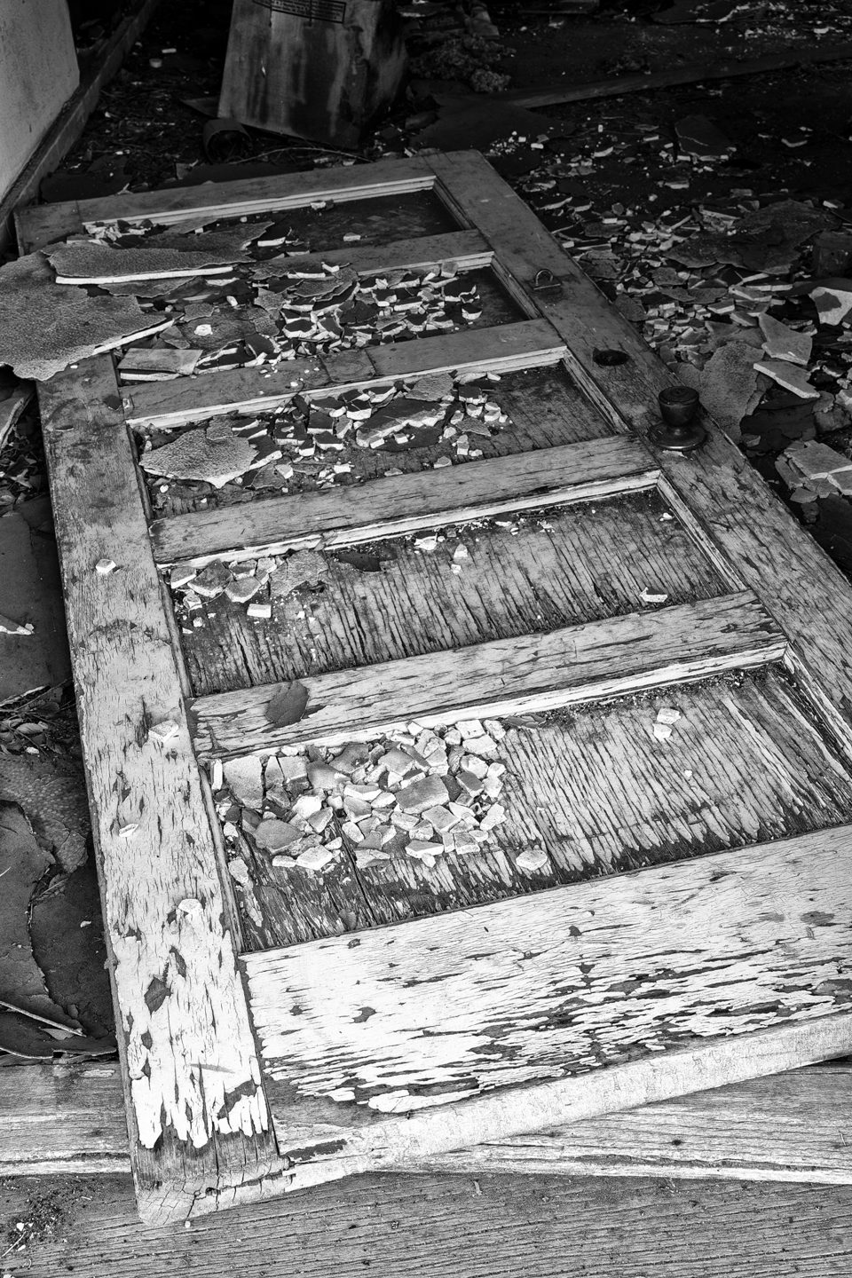 Black and white photograph of a door fallen onto the floor of a motel room in the abandoned Texas Longhorn Motel in the ghost town of Glenrio, on the Texas / New Mexico state line.