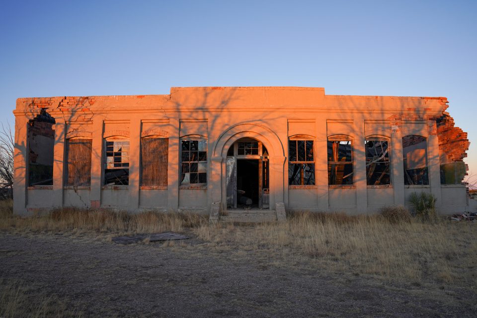 The morning sunrise blazed orange on the front of the dilapidated old school building in Cedarvale, New Mexico.