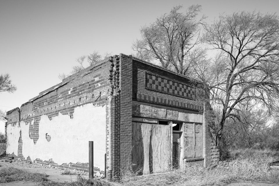 Black and white photograph of an abandoned building along Route 66 on the corner of Grand and Broadway in Texola, Oklahoma. This was a grocer and general merchandise store. It can be seen on the vintage 1905 map in the video.