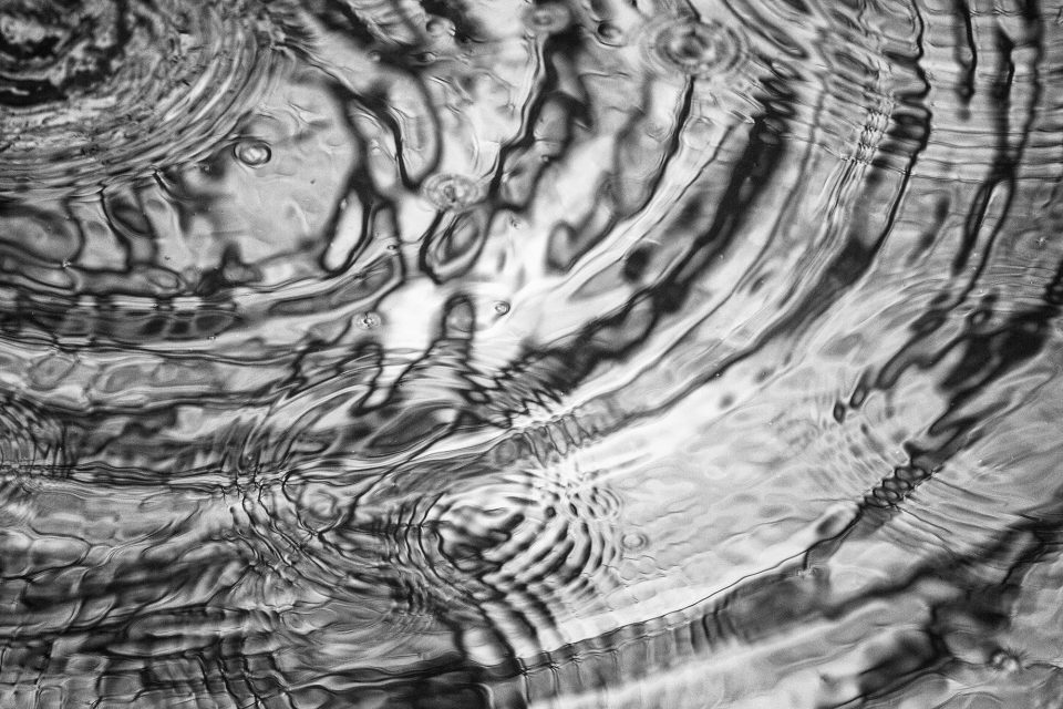 Black and white photograph of ripples in a puddle of water created by raindrops, by Keith Dotson.