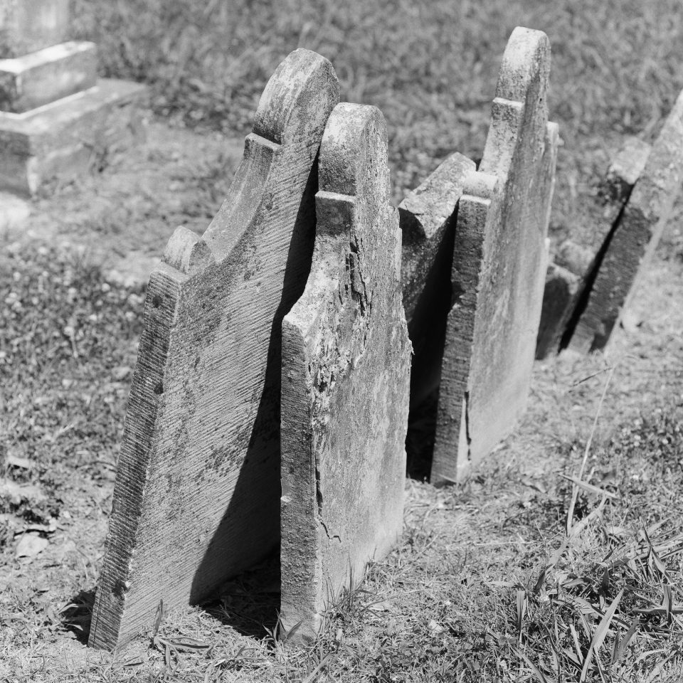 Leaning headstones. Black and white photograph by Keith Dotson, shot with Hasselblad 500 C/M, with Cinestill Double X BwXX film.
