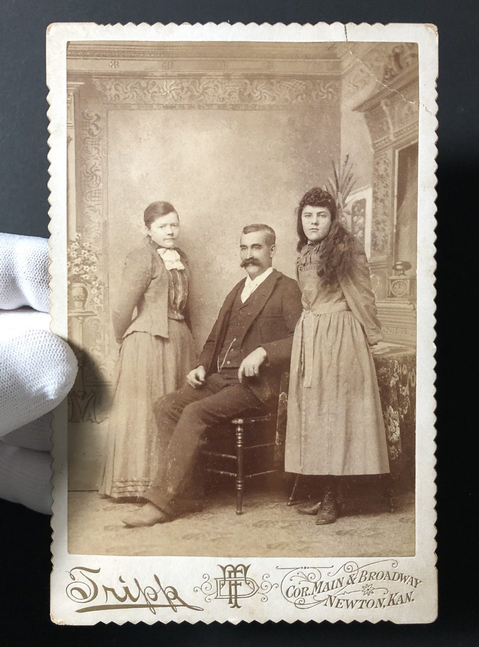 This unidentified family posed in the studio of Frank D. Tripp at the corner of Main Street and Broadway in Newton, Kansas, likely in the late 1880s. The backdrop was a painted scene.
