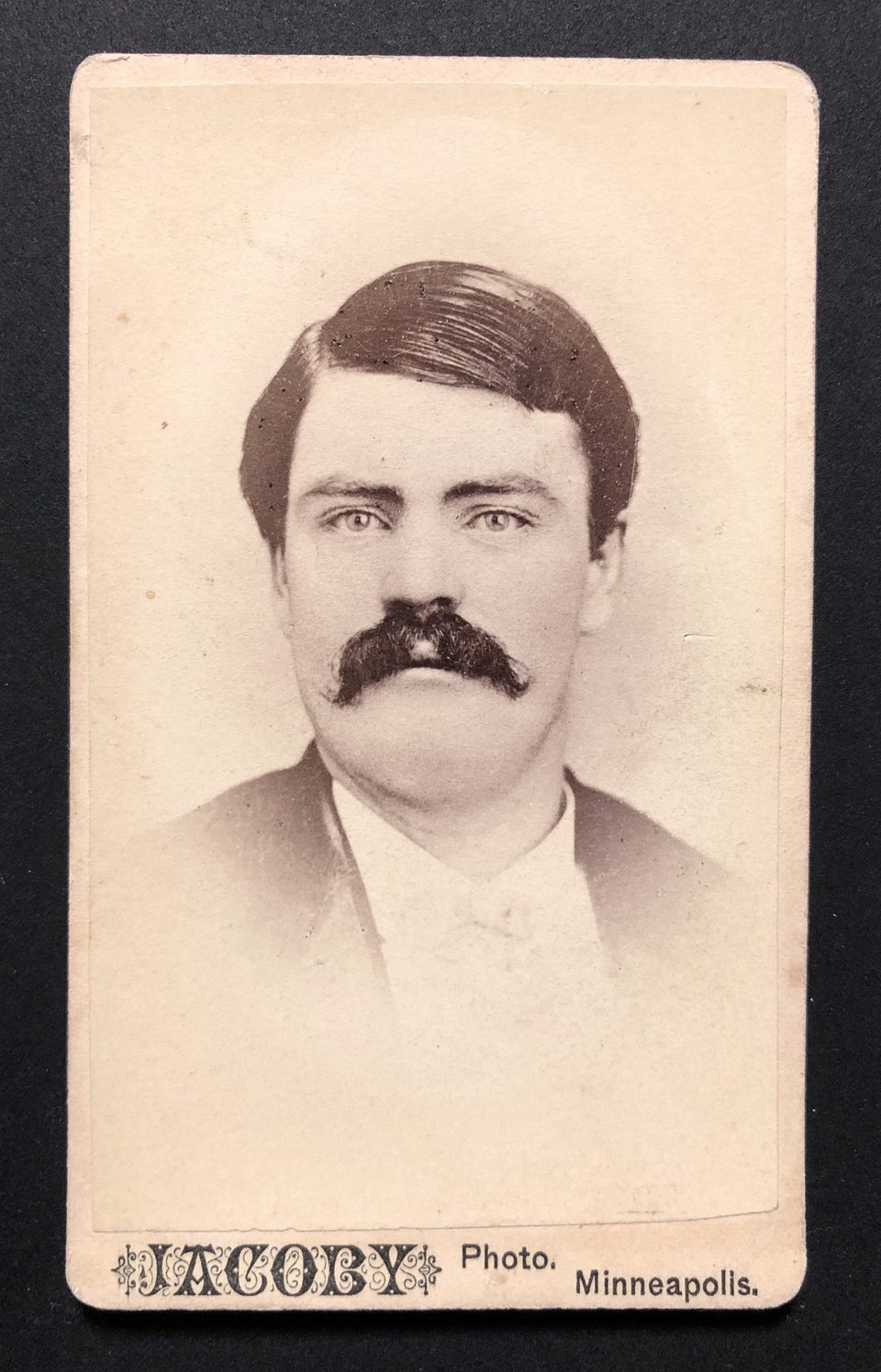 Carte de visite portrait of a man with a thick mustache. In this portrait, the edges vignette away to white. The photographer's name appears on the front, with the verso blank.