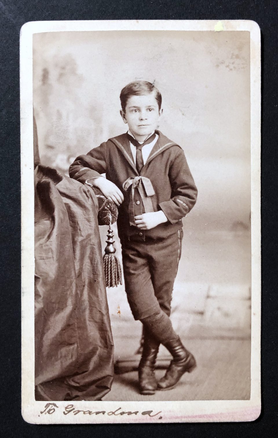 Carte de visite size portrait by John H. Oleson of a young boy in a suit and boots, presumably the older brother of the baby shown above. This photo has a matching inscription on the bottom edge in pen and ink, "To Grandma." 