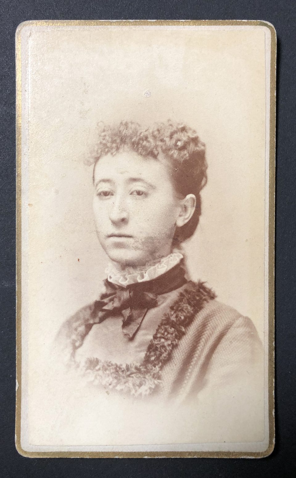 Head and shoulders portrait of a young woman made by photographer J.A. Brush. The edge of the card is lined with metallic gold.
