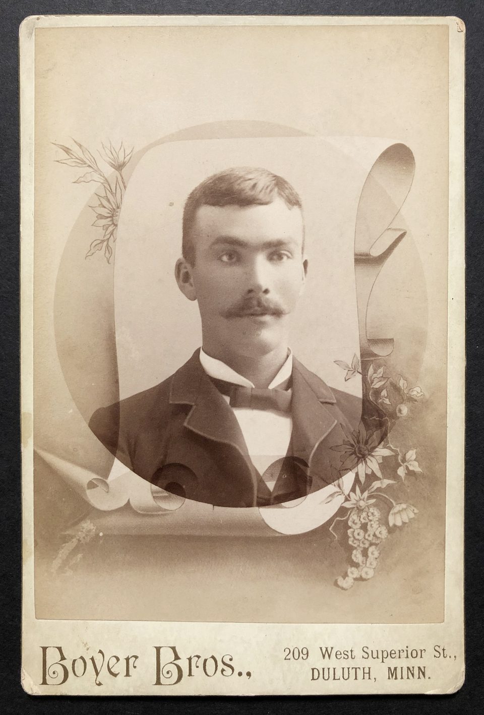 Cabinet card portrait of a young man with a mustache wearing a bow tie, by the studio of Boyer Brothers, located at 209 West Superior Street, in Duluth, Minnesota, possibly 1890s.