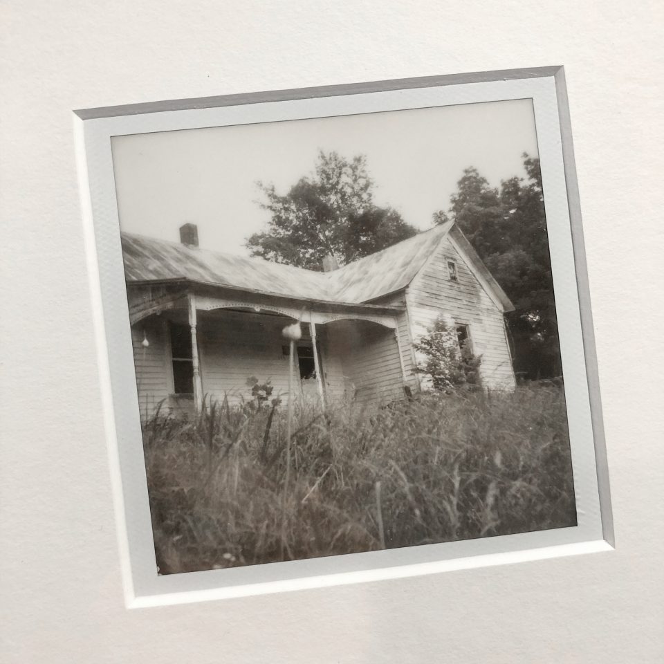 Close-up look at the original Polaroid print of the Hollow Rock farmhouse in the mat window. Reflections are visible in the protective acid sleeve.