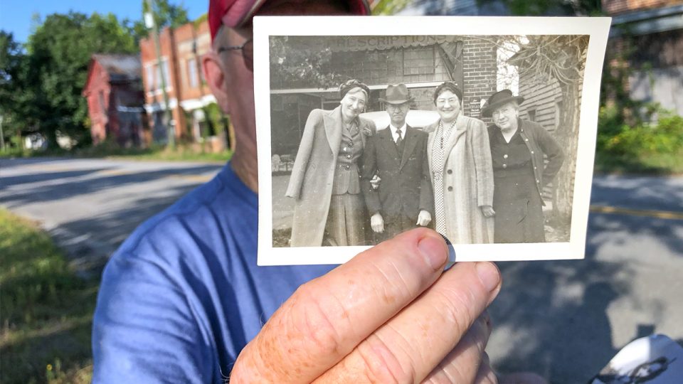 Jimmy Thompson holding a historic photograph of Union Level pharmacist and drug store owner C.P. Jones, whose name is still visible on the front of his store. On his right arm is his wife. The other two women are unidentified.