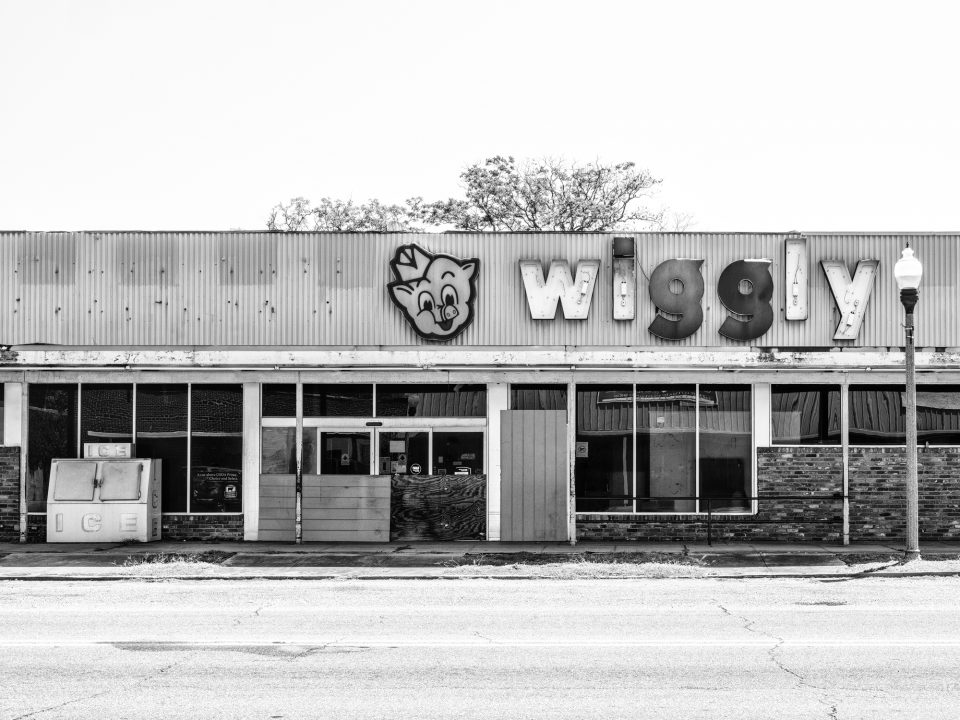 A defunct Piggly Wiggly grocery store with only part of its sign still intact. Black and white photograph by Keith Dotson.
