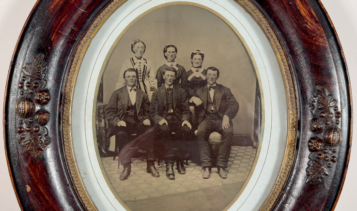 Tintype portrait of a group of six well-dressed young people, three brothers and their three sisters, with a thin paper mat and an ornate antique oval picture frame.