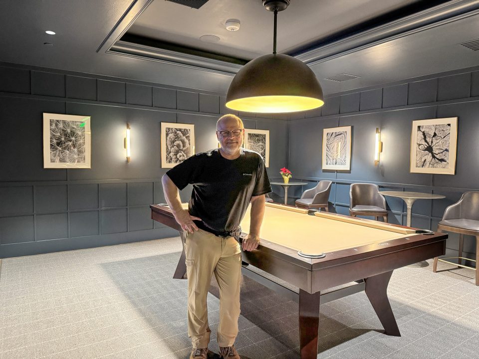 Portrait of Keith Dotson, surrounded by a collection of his black and white photographs, in the billiard room of the newly remodeled Sam Houston Hotel.