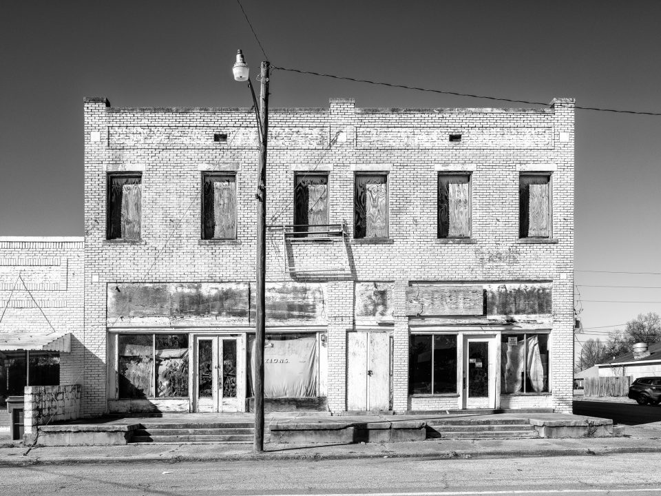 Big, two story vacant storefront in Hughes, Arkansas. Black and white photograph by Keith Dotson.