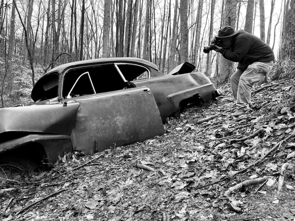 Photographer Keith Dotson shoots an old car in the woods. Photo by Teena Young.