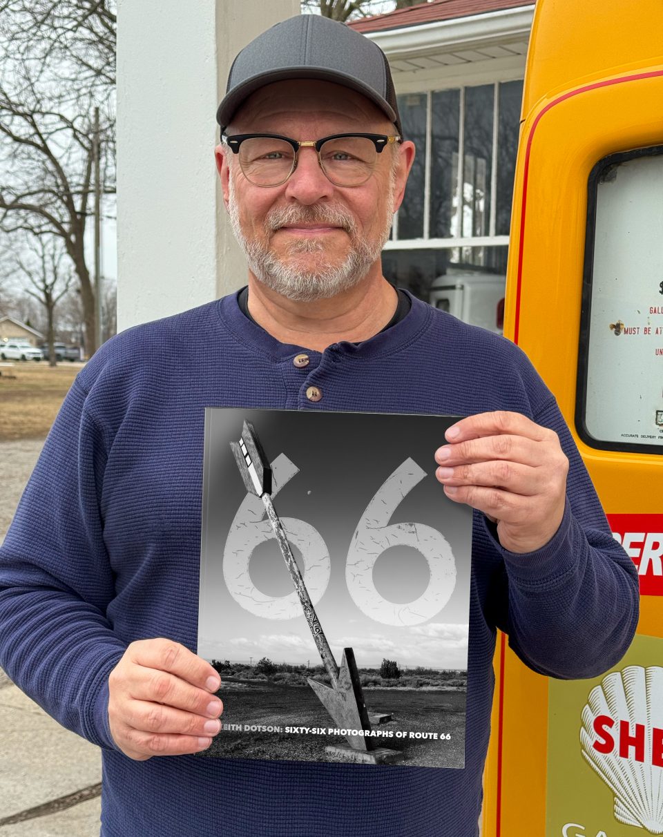 Photographer Keith Dotson seen holding a copy of his new book Sixty-Six Photographs of Route 66 on the Route 66 location of Soulsby's Service Station in Illinois. Photo by Teena Young. 