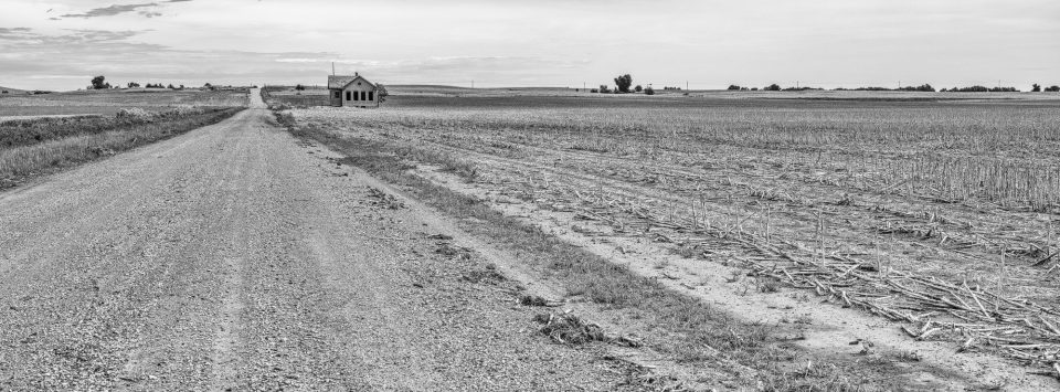 Panoramic view of the Kansas prairie with an abandoned one-room schoolhouse on the horizon.