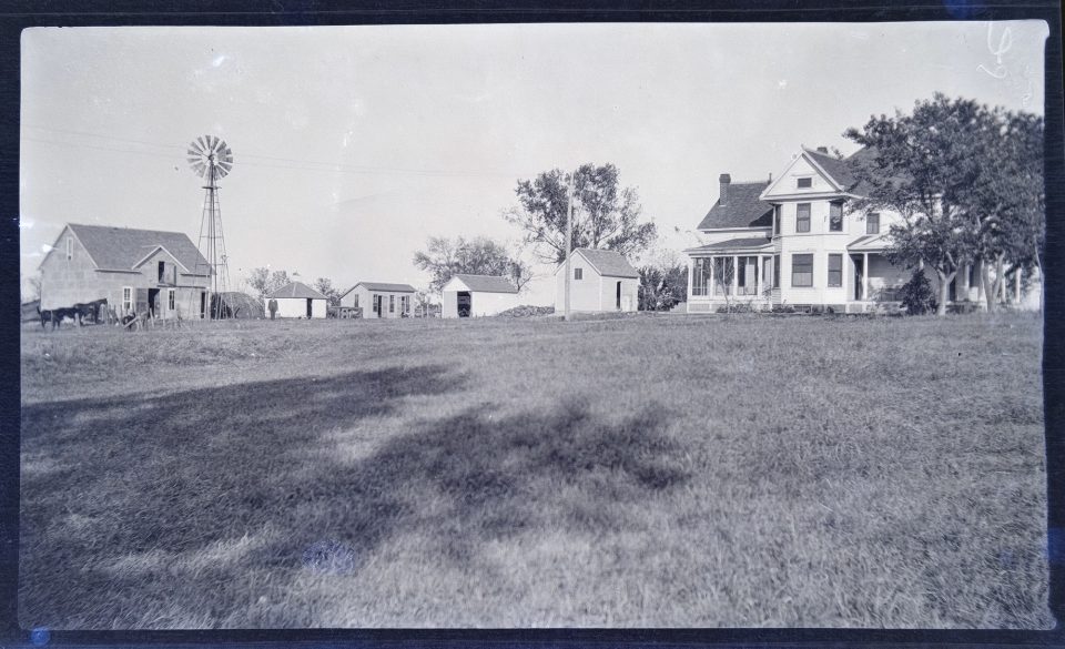 A wide photograph of the farmhouse and farm buildings.