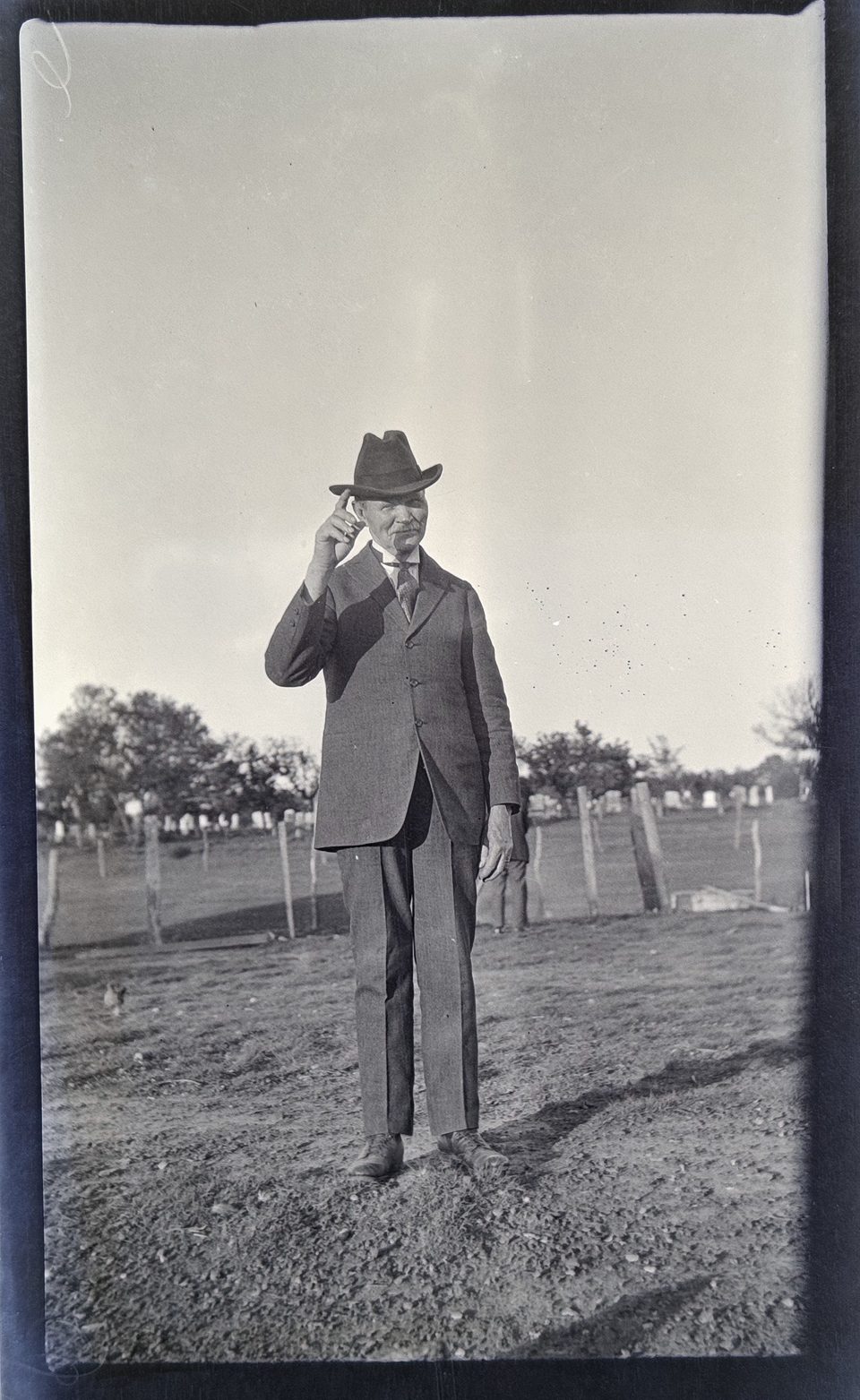 Portrait of an elderly man in his dress suit and stetson hat with a cemetery visible in the background.