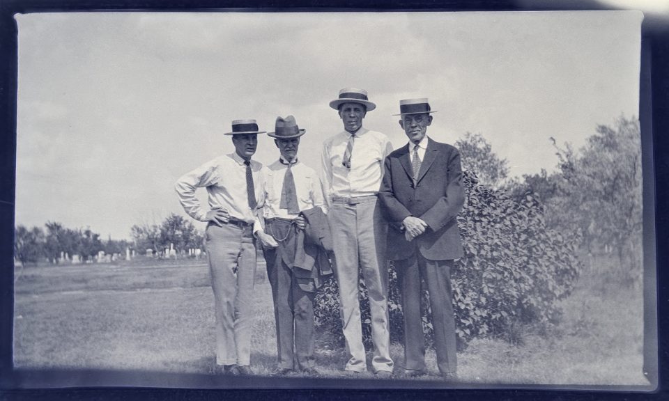 A group of men at the cemetery. Straw boater hats reached their "golden age" of peak popularity from the late 1890s until the 1920s. AI estimated the timeframe of this photograph to be the 1910s to 1920.