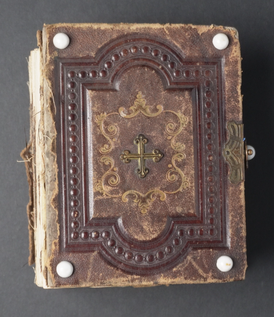 Decorative leather cover of an antique family photo album from Ohio featuring embossing, gold foil details, a brass cross in the center, and white milk glass buttons designed to help the book avoid excess wear.